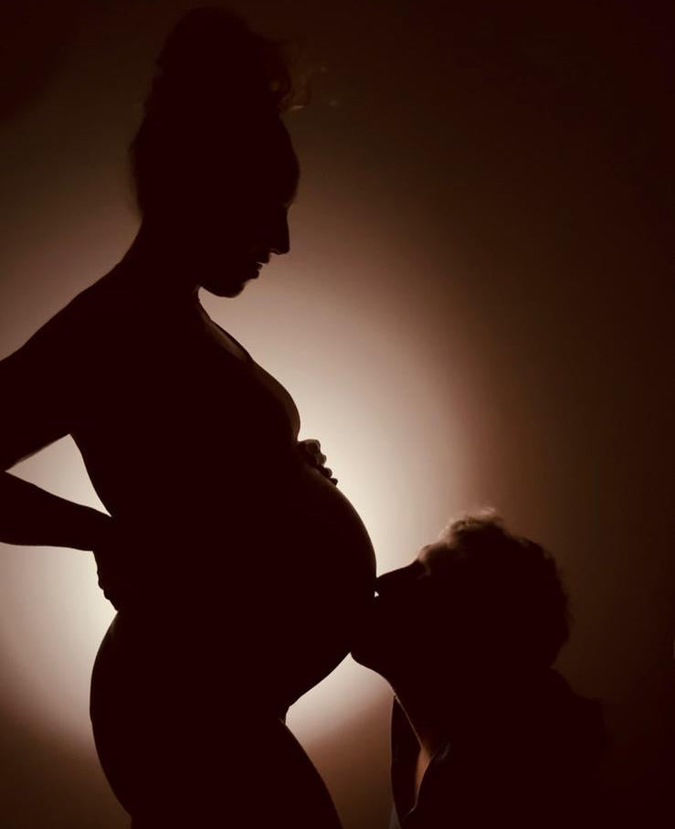 Silhouette of a pregnant woman and a child against a dark background with a warm light source.